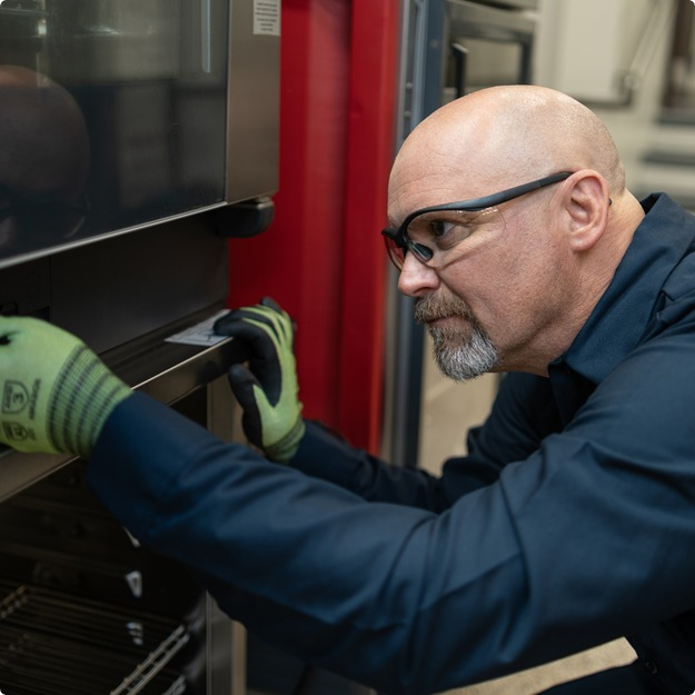Service technician in safety glasses and work gloves servicing a commercial oven