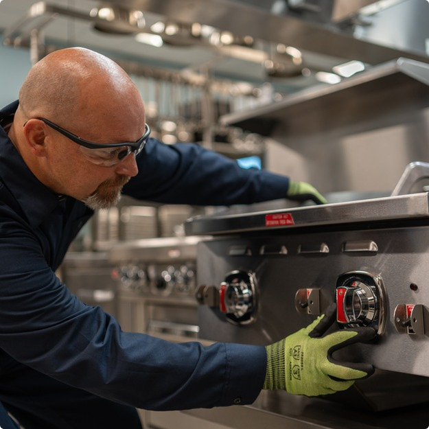 Service technician in safety glasses adjusting the control knobs on a commercial range