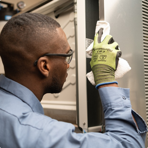 Service technician in safety glasses and work gloves cleaning a commercial equipment component during installation