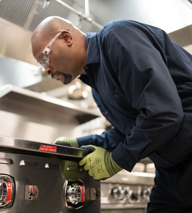 Service technician in safety glasses and work gloves leaning in to inspect a commercial range