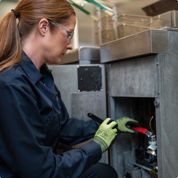Service technician in safety glasses using a screwdriver on an equipment control panel