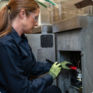Service technician in safety glasses using a screwdriver on an equipment control panel