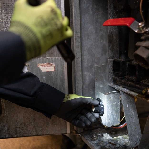 Gloved hands using a flashlight to inspect the inside of commercial equipment