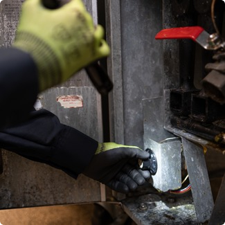 Gloved hands using a flashlight to inspect the inside of commercial equipment