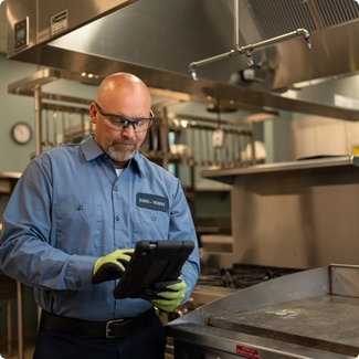 Commercial kitchen service technician in a blue uniform reviewing a work order on a tablet