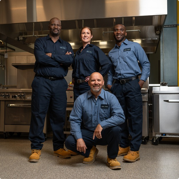 Team of four commercial kitchen service technicians in uniform posing together in a restaurant kitchen