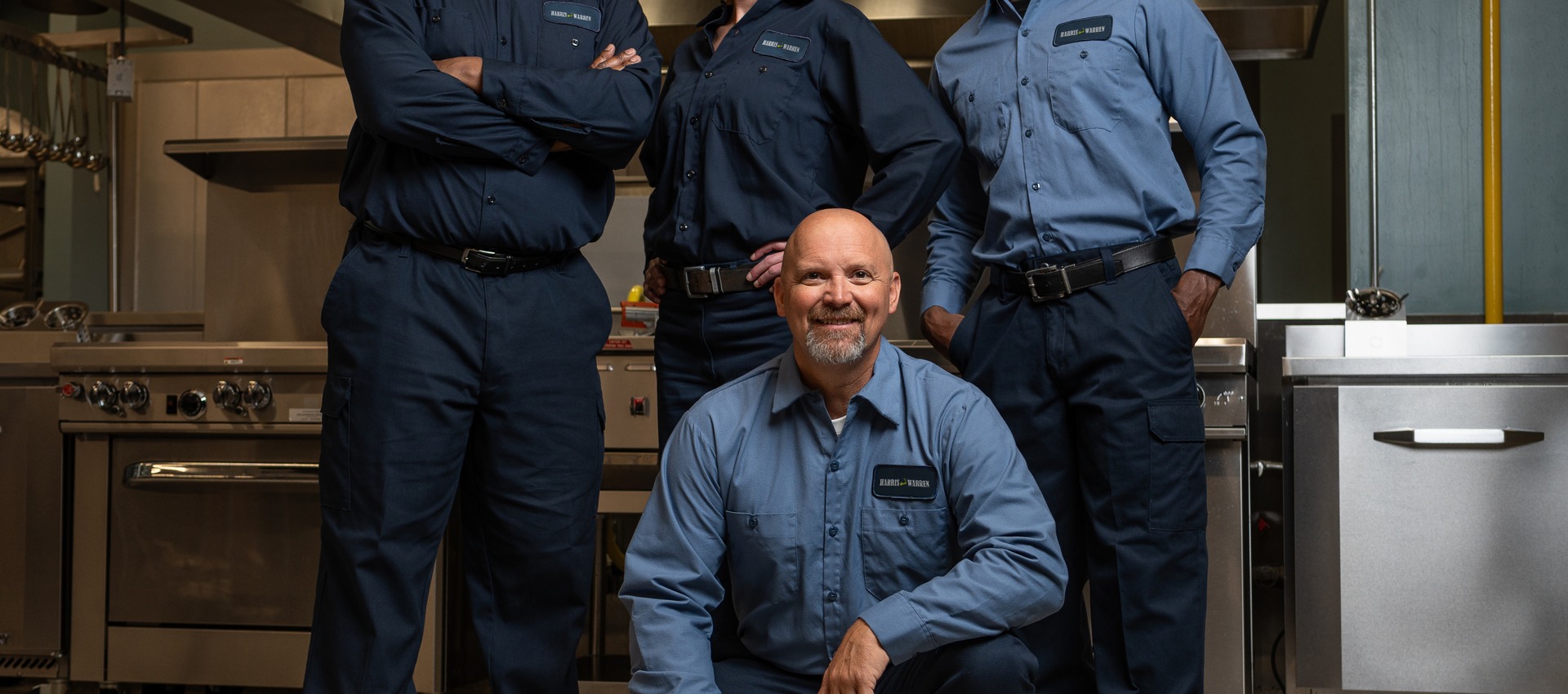 Team of four commercial kitchen service technicians in uniform posing together in a restaurant kitchen