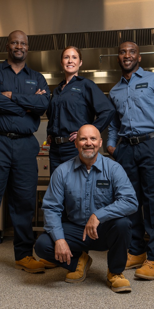Team of four commercial kitchen service technicians in uniform posing together in a restaurant kitchen