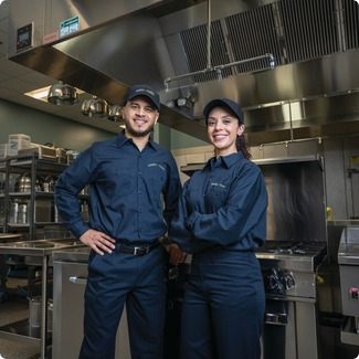 Two commercial kitchen service technicians in uniform standing among cooking equipment