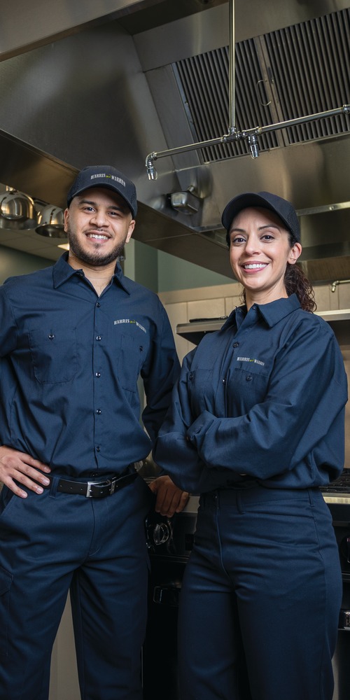 Two commercial kitchen service technicians in uniform standing among cooking equipment