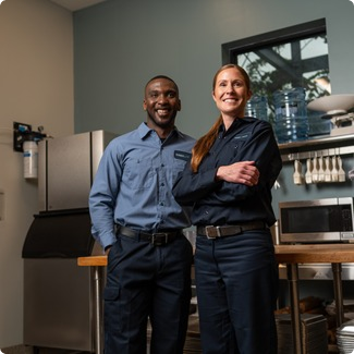 Two smiling commercial kitchen service technicians in uniform standing with arms crossed