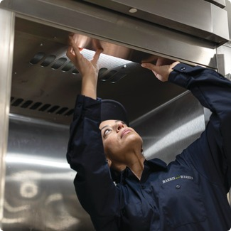 Service technician reaching up to work on a stainless steel commercial kitchen hood