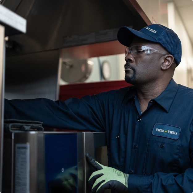 Service technician in a cap and work gloves inspecting a commercial dishwasher