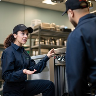 Service technician talking through a repair with a colleague in a commercial kitchen