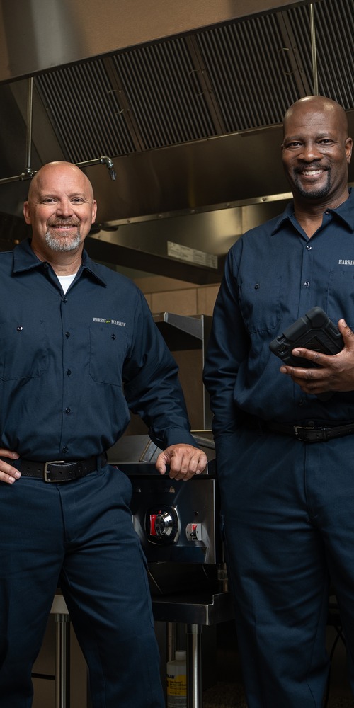 Two commercial kitchen service technicians in uniform standing in a restaurant kitchen
