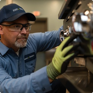 Commercial kitchen service technician in safety glasses and gloves inspecting a component of commercial bakery equipment