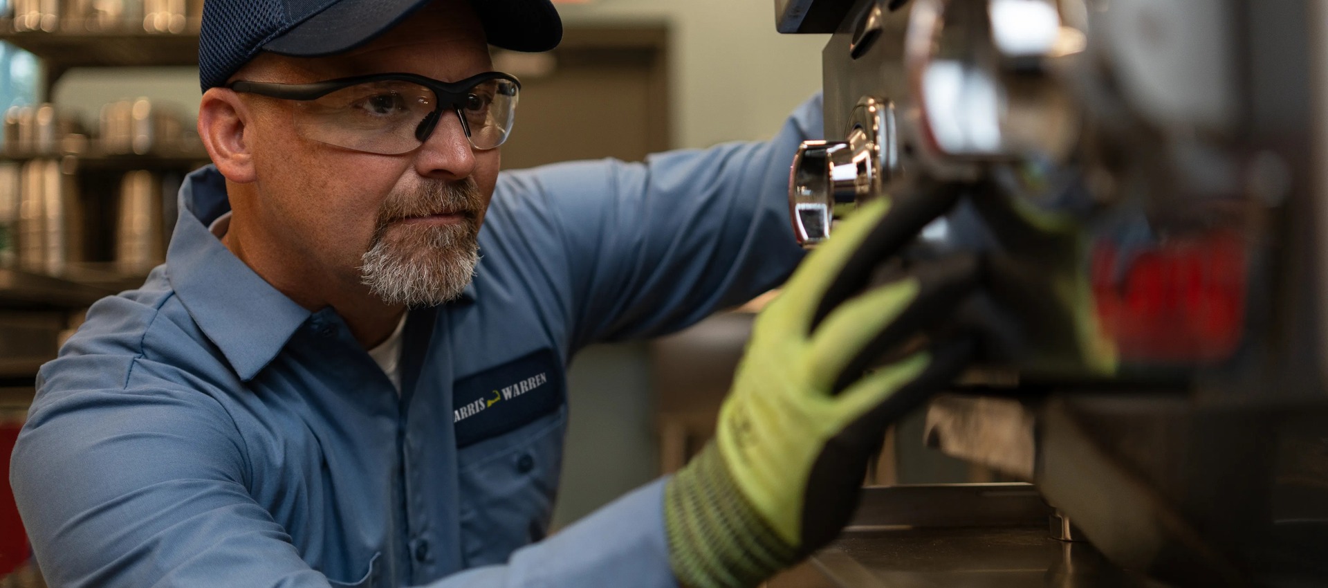 Commercial kitchen service technician in safety glasses and gloves inspecting a component of commercial bakery equipment