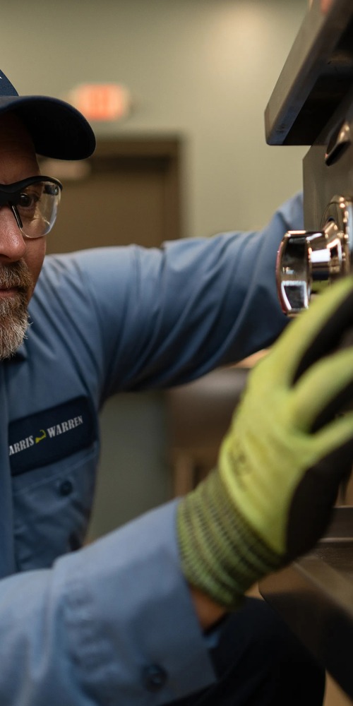 Commercial kitchen service technician in safety glasses and gloves inspecting a component of commercial bakery equipment