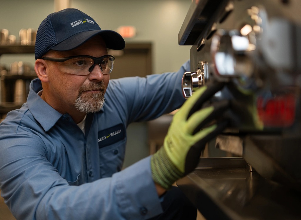 Commercial kitchen service technician in safety glasses and gloves inspecting a component of commercial bakery equipment