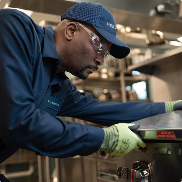 Service technician in a cap and work gloves repairing commercial kitchen equipment