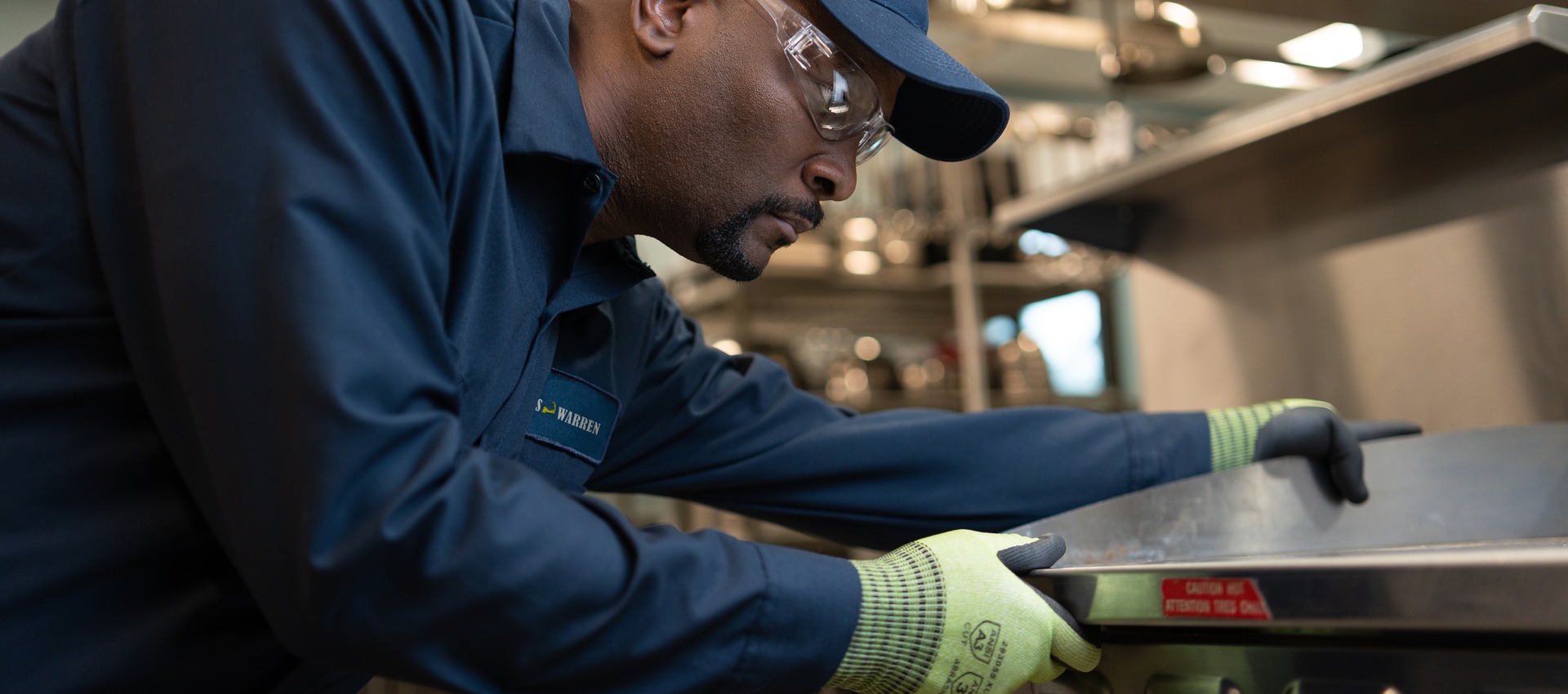 Service technician in a cap and work gloves repairing commercial kitchen equipment