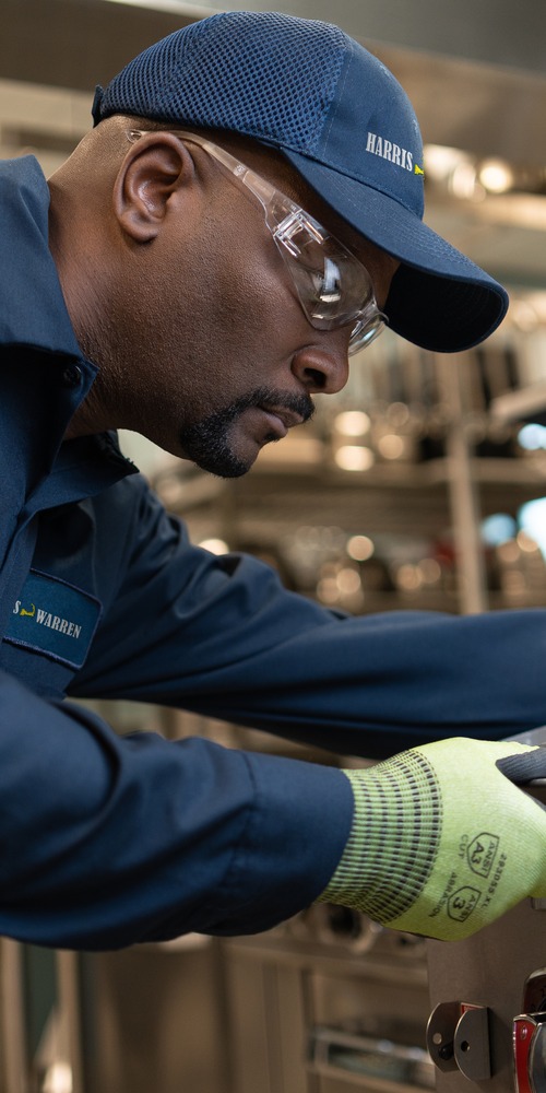 Service technician in a cap and work gloves repairing commercial kitchen equipment