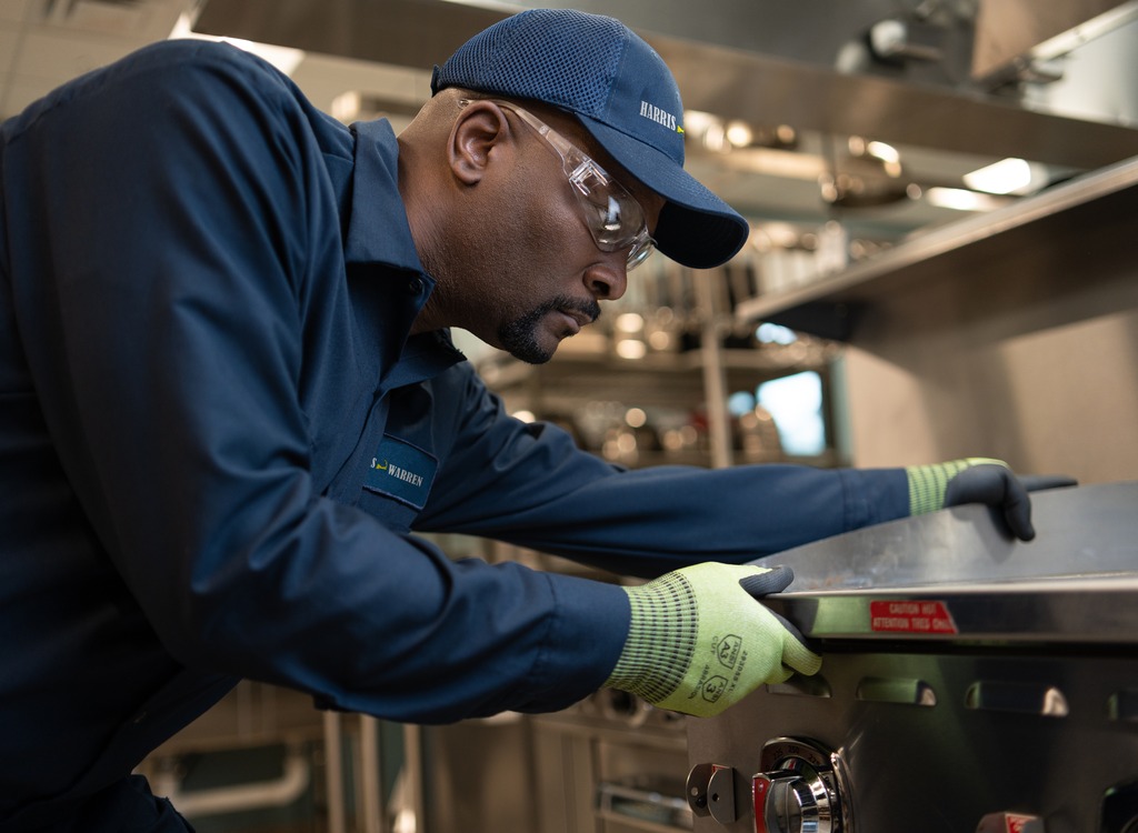 Service technician in a cap and work gloves repairing commercial kitchen equipment