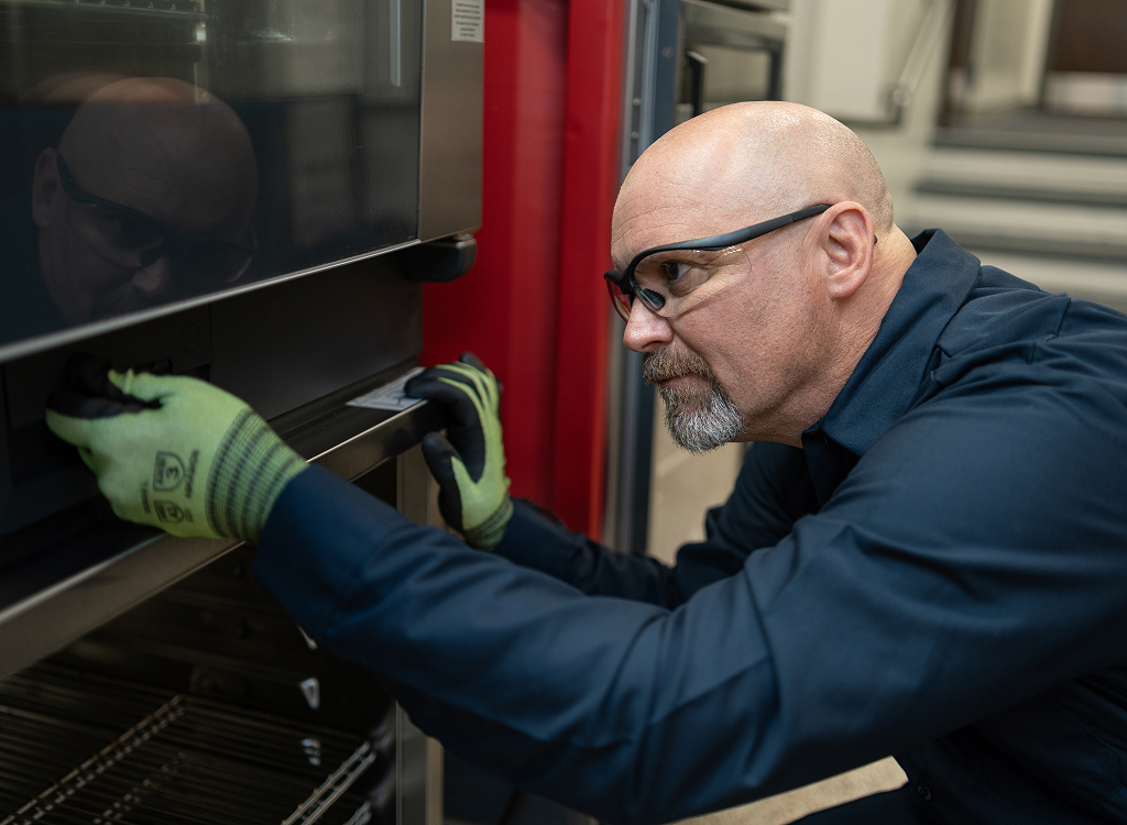 Service technician in safety glasses and work gloves servicing a commercial oven