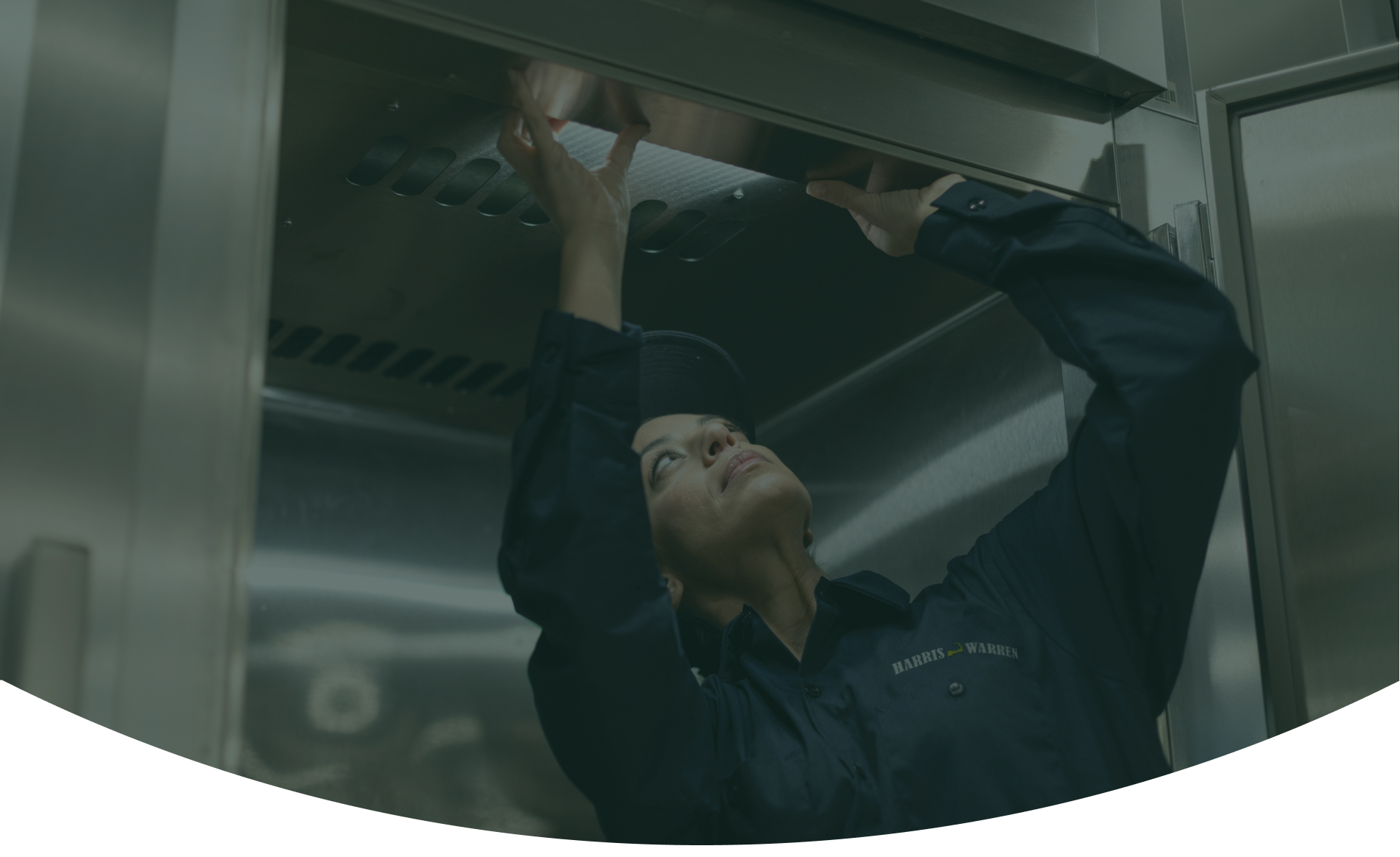Service technician reaching up to work on a commercial kitchen exhaust hood
