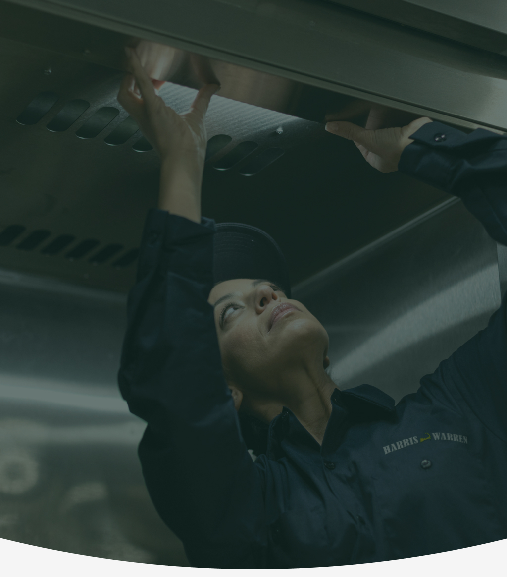 Service technician reaching up to work on a commercial kitchen exhaust hood